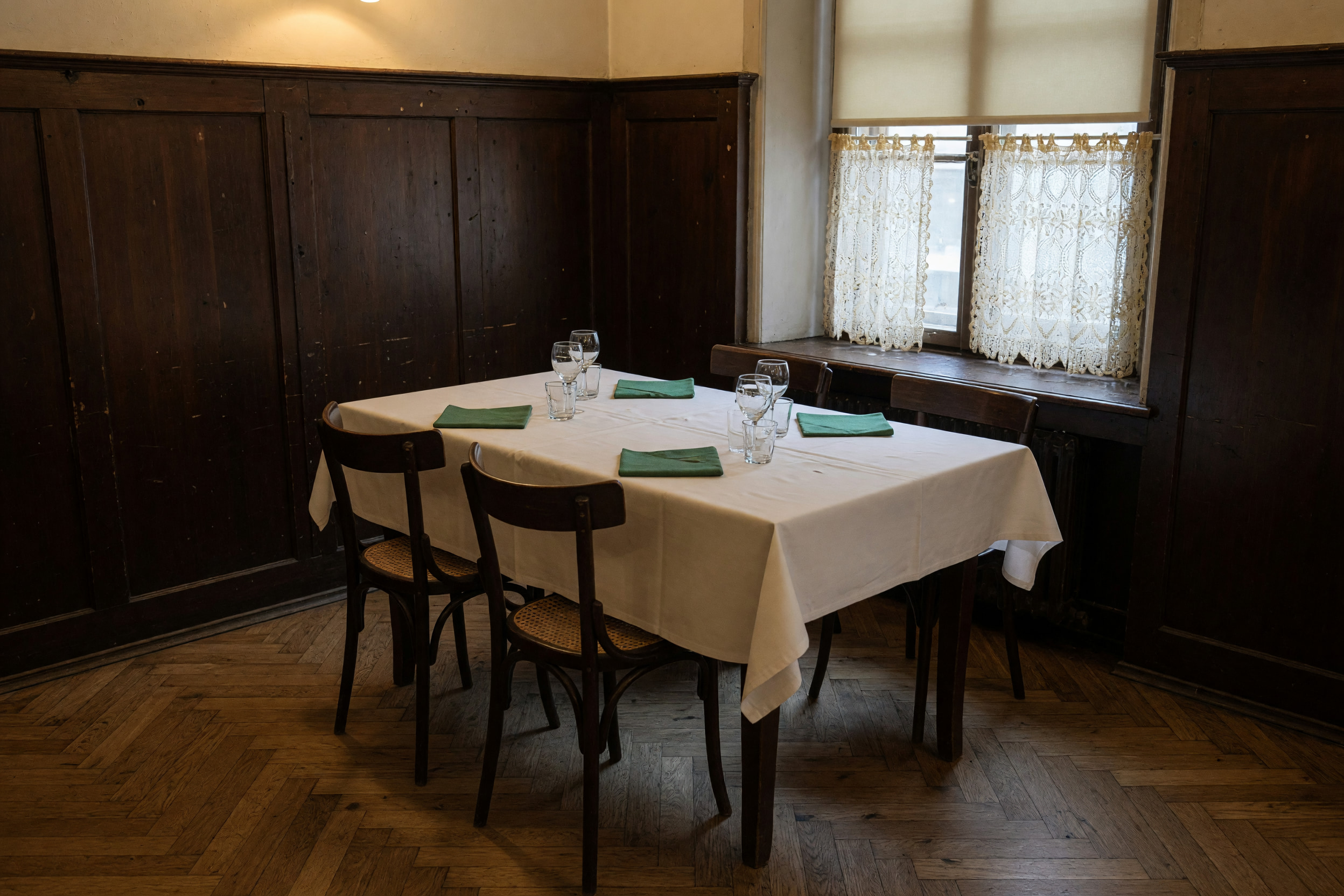 Gedeckter Tisch mit weißem Leinen und grünen Stoffservietten im holzvertäfelten Speisesaal des Wirtshauses